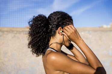 Nahaufnahme einer Sportlerin, die ein Headset einstellt, während sie vor einem blauen Himmel steht - CAVF49039