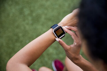 High angle view of female athlete using smart watch while standing on grassy field - CAVF49060