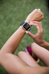 High angle view of female athlete using smart watch while sitting on grassy field - CAVF49061
