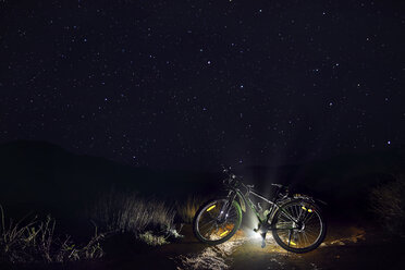 Mountainbike mit beleuchtetem Licht gegen Sternenfeld in der nächtlichen Wüste - CAVF49090