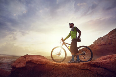In voller Länge von Wanderer mit Mountainbike stehen auf Felsen gegen den Himmel in der Wüste bei Sonnenuntergang - CAVF49092