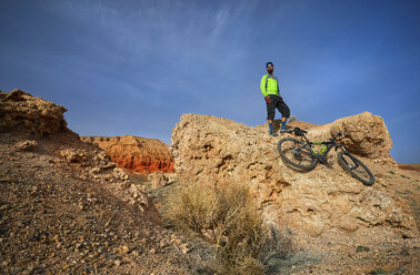 Low angle view of Wanderer stehend auf Felsformation mit Mountainbike in der Wüste - CAVF49095