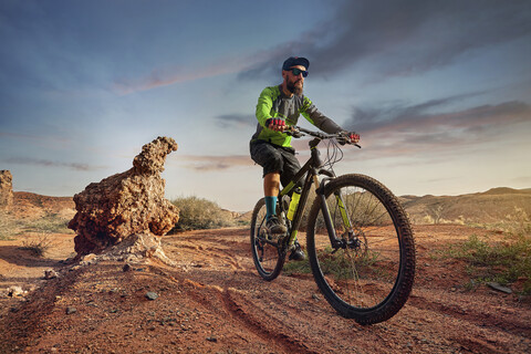 Wanderer Mountainbiken in der Wüste gegen den Himmel bei Sonnenuntergang, lizenzfreies Stockfoto