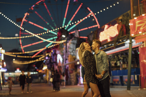 Happy young couple embracing and kissing at a funfair - LHPF00116