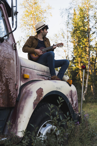 Ein junger Mann sitzt auf einem kaputten Lastwagen und spielt Ukulele, lizenzfreies Stockfoto