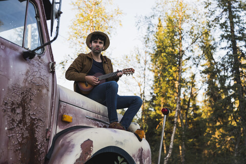 Ein junger Mann sitzt auf einem kaputten Lastwagen und spielt Ukulele, lizenzfreies Stockfoto