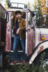 Cool young man standing in cabin of a broken truck - KKAF02186