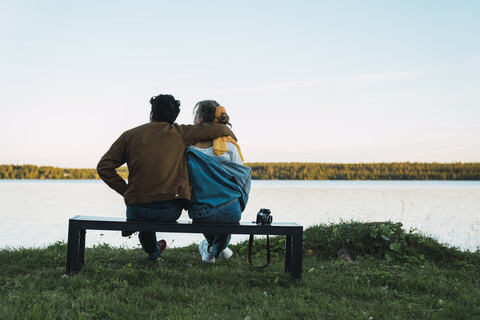 Junges Paar sitzt auf einer Bank und schaut auf den See, lizenzfreies Stockfoto