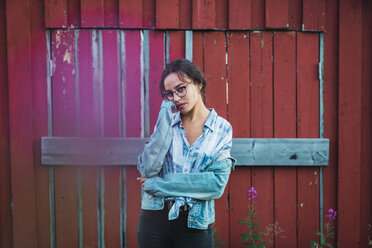 Portrait of a young woman standing in front of a red wood hut - KKAF02216