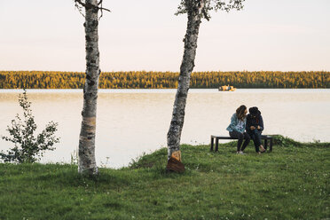 Junges Paar sitzt auf einer Bank in der Nähe eines Sees und prüft Bilder auf einer Kamera - KKAF02230