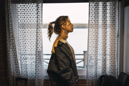 Porträt einer jungen Frau, die in einem Raum mit einem Fenster steht - KKAF02232