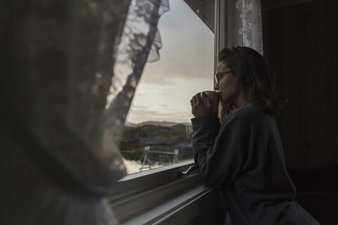 Junge Frau schaut aus dem Fenster und trinkt Tee, lizenzfreies Stockfoto