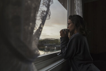 Junge Frau schaut aus dem Fenster und trinkt Tee - KKAF02236