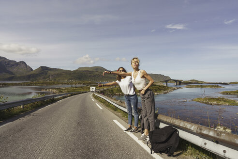 Junge Frauen, die auf einer leeren Straße trampen, Lappland, Norwegen - KKAF02242