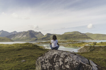 Junge Frau auf einem Felsen sitzend, mit Blick auf die Aussicht, meditierend, Lappland, Norwegen - KKAF02243