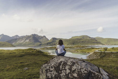 Young woman sitting on a rock, looking at view, meditating, Lapland, Norway - KKAF02243