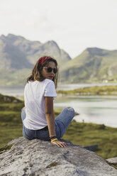 Junge Frau auf einem Felsen sitzend, mit Blick auf die Aussicht, Lappland, Norwegen - KKAF02244