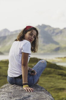 Junge Frau auf einem Felsen sitzend, mit Blick auf die Aussicht, Lappland, Norwegen - KKAF02245