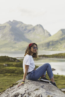 Junge Frau auf einem Felsen sitzend, mit Blick auf die Aussicht, Lappland, Norwegen - KKAF02249