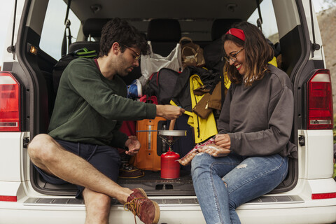 Junges Paar bereitet Würstchen auf einem Campingkocher zu, lizenzfreies Stockfoto