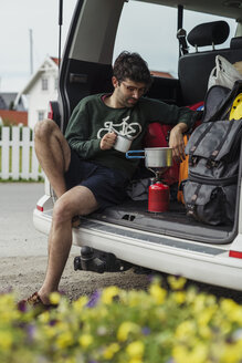 Junger Mann sitzt im Wohnmobil und bereitet Kaffee auf einem Campingkocher zu - KKAF02258
