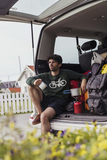 Junger Mann sitzt im Wohnmobil und bereitet Kaffee auf einem Campingkocher zu - KKAF02259