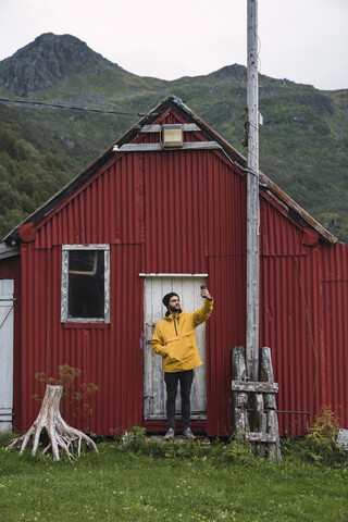 Junger Mann steht vor einer Wellblechhütte und macht ein Selfie, lizenzfreies Stockfoto