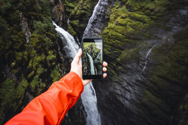 Person, die mit ihrem Smartphone ein Foto von einem Wasserfall macht, Lappland, Norwegen - KKAF02285
