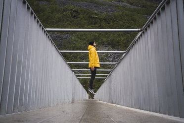 Junger Mann mit einem Regenmantel, der auf eine Brücke springt - KKAF02288