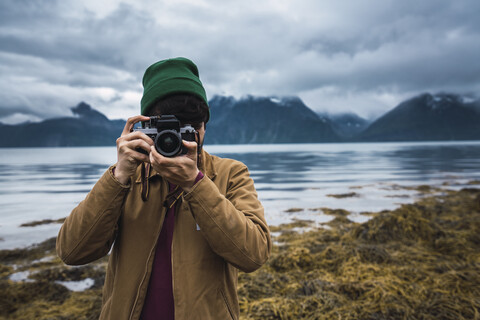 Young man with woolly hat taking pictures with camera stock photo
