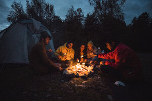 Eine Gruppe von Freunden sitzt an einem Lagerfeuer und röstet Marshmallows - KKAF02293