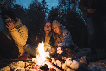 Eine Gruppe von Freunden sitzt an einem Lagerfeuer und röstet Marshmallows - KKAF02295