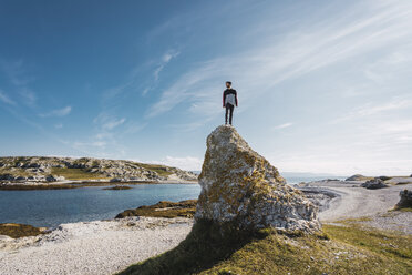 Finland, Lapland, man standing on top of a rock at the coast - KKAF02314