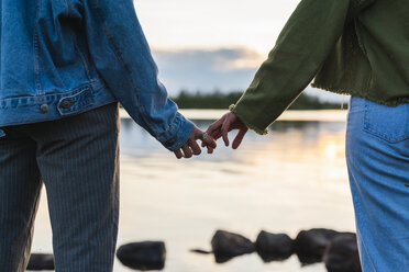 Finland, Lapland, close-up of two young women hand in hand at the lakeside at twilight - KKAF02323