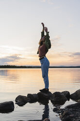 Finland, Lapland, woman standing at the lakeside at twilight - KKAF02334