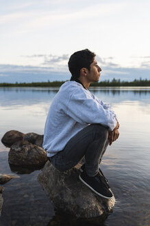Finnland, Lappland, Mann sitzt auf einem Felsen in einem See - KKAF02338