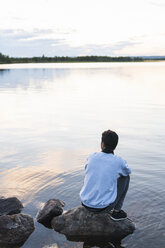 Finnland, Lappland, Mann sitzt auf einem Felsen in einem See - KKAF02339