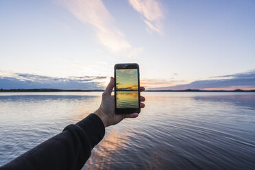 Finland, Lapland, man taking cell phone picture of stunning lake at twilight - KKAF02341