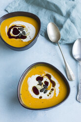 Two bowls of homemade Hokkaido pumpkin soup garnished with cream, pumpkin seed oil and pumpkin seed - JUNF01351