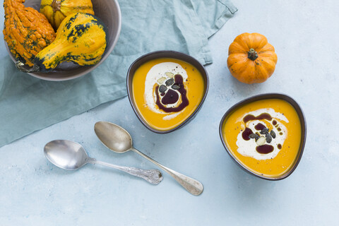 Zwei Schalen mit hausgemachter Hokkaido-Kürbissuppe, garniert mit Sahne, Kürbiskernöl und Kürbiskernen, lizenzfreies Stockfoto