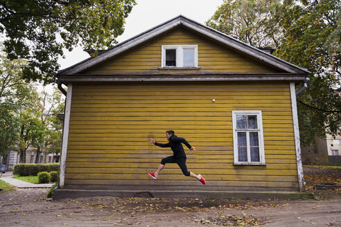 Dynamic athlete jumping in front of a yellow wood house - KKAF02350