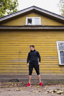 Sportler vor einem gelben Holzhaus stehend - KKAF02351
