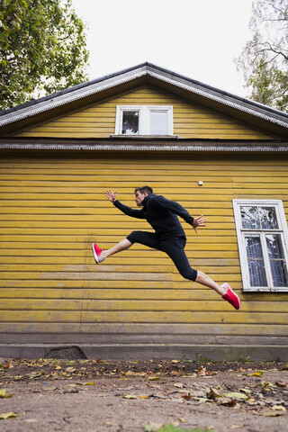 Dynamischer Athlet, der vor einem gelben Holzhaus springt, lizenzfreies Stockfoto