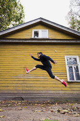 Dynamic athlete jumping in front of a yellow wood house - KKAF02352