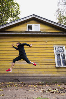 Dynamischer Athlet, der vor einem gelben Holzhaus springt - KKAF02353