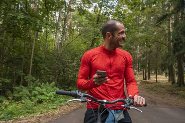 Mountainbiker mit Smartphone im Wald - KKAF02355