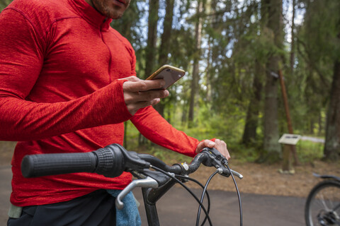 Mountainbiker mit Smartphone im Wald, lizenzfreies Stockfoto