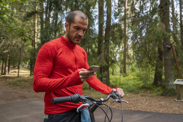 Mountainbiker mit Smartphone im Wald - KKAF02357