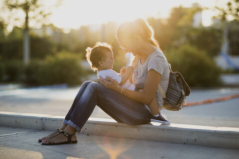 Glückliche Mutter sitzt mit ihrem kleinen Sohn auf einem Platz bei Sonnenuntergang, lizenzfreies Stockfoto