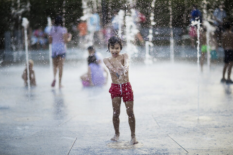 Unbekümmerter Junge spielt mit Wasser aus einem Brunnen, lizenzfreies Stockfoto